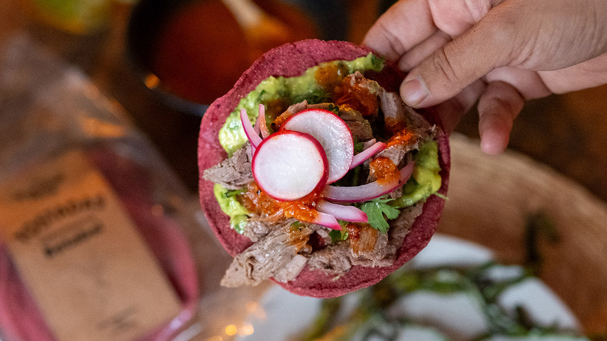 Receta de tostadas de betabel con arrachera, guacamole, cebolla encurtida, rábano, cilantro y limón sobre tostadas horneadas.